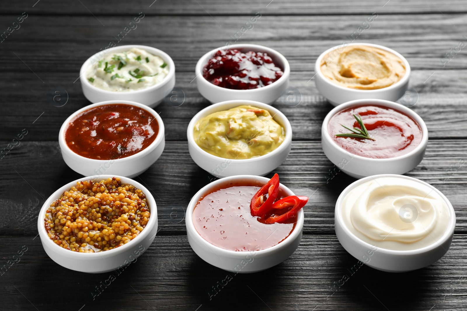 Photo of Different tasty sauces in bowls on black wooden table