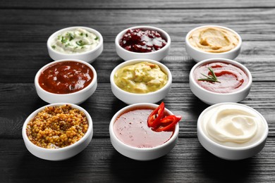 Photo of Different tasty sauces in bowls on black wooden table