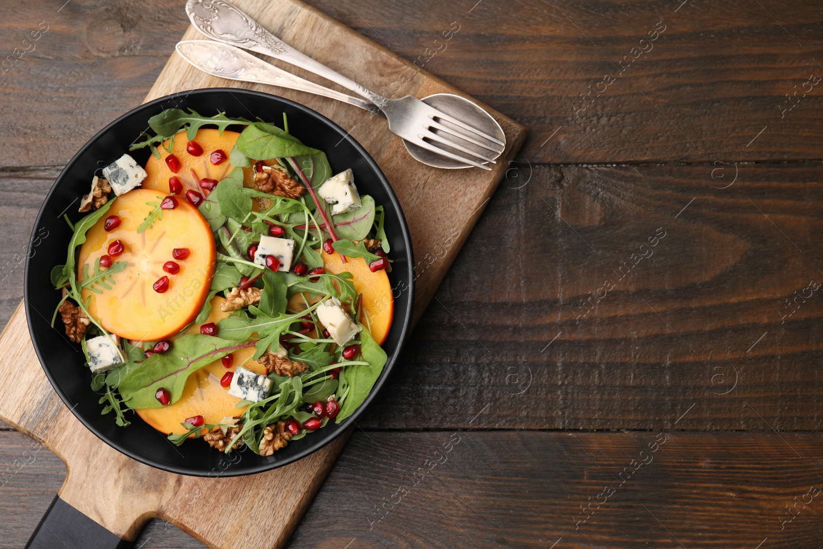 Photo of Tasty salad with persimmon, blue cheese, pomegranate and walnuts served on wooden table, top view. Space for text