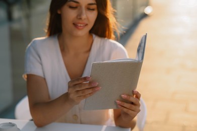 Photo of Young woman reading book in outdoor cafe on sunny day
