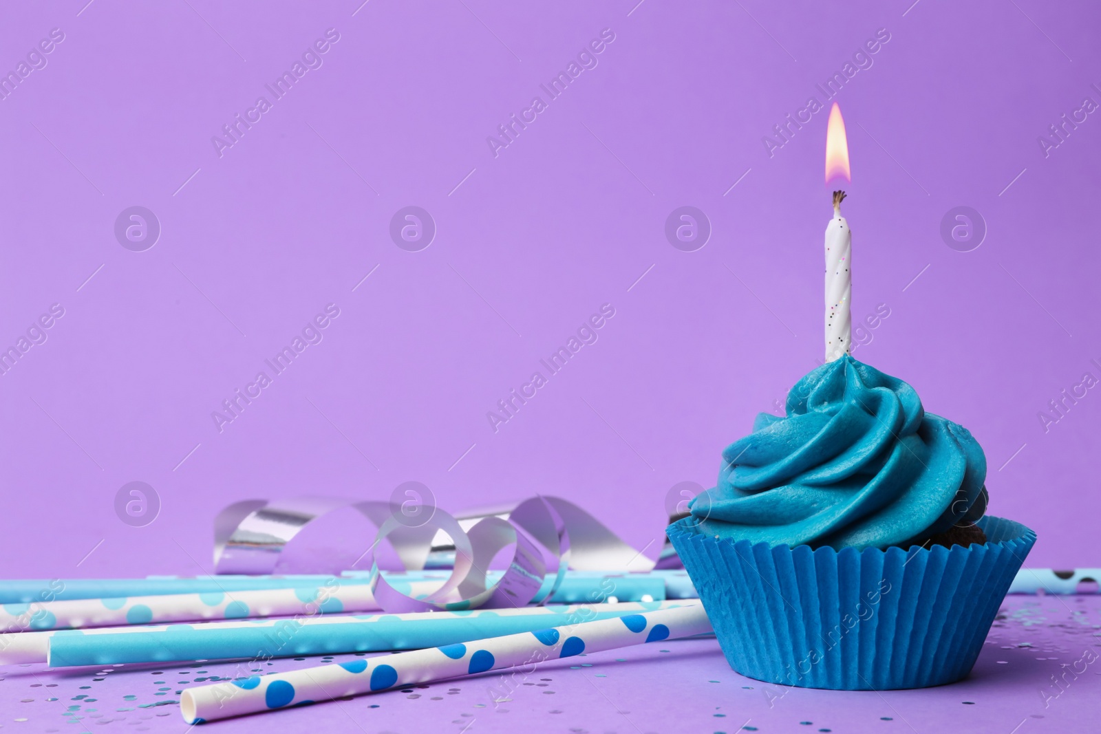 Photo of Delicious birthday cupcake with blue cream and burning burning candle on violet background. Space for text