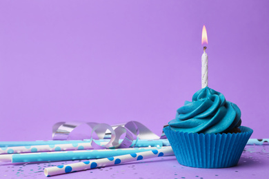 Delicious birthday cupcake with blue cream and burning burning candle on violet background. Space for text