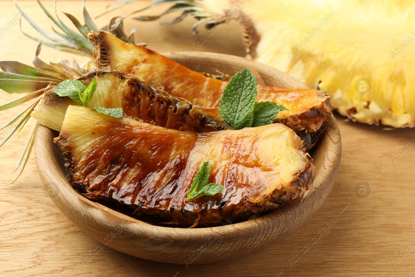 Photo of Tasty grilled pineapples in bowl on wooden table, closeup