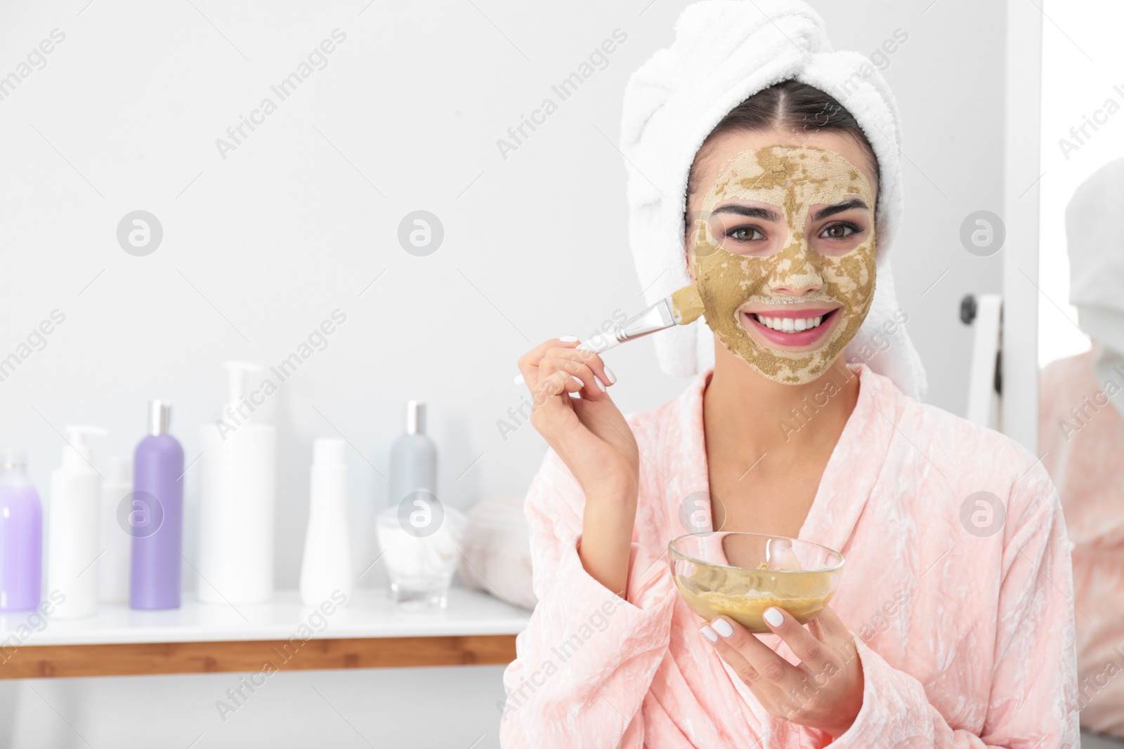 Photo of Young woman applying clay mask on her face in bathroom, space for text. Skin care