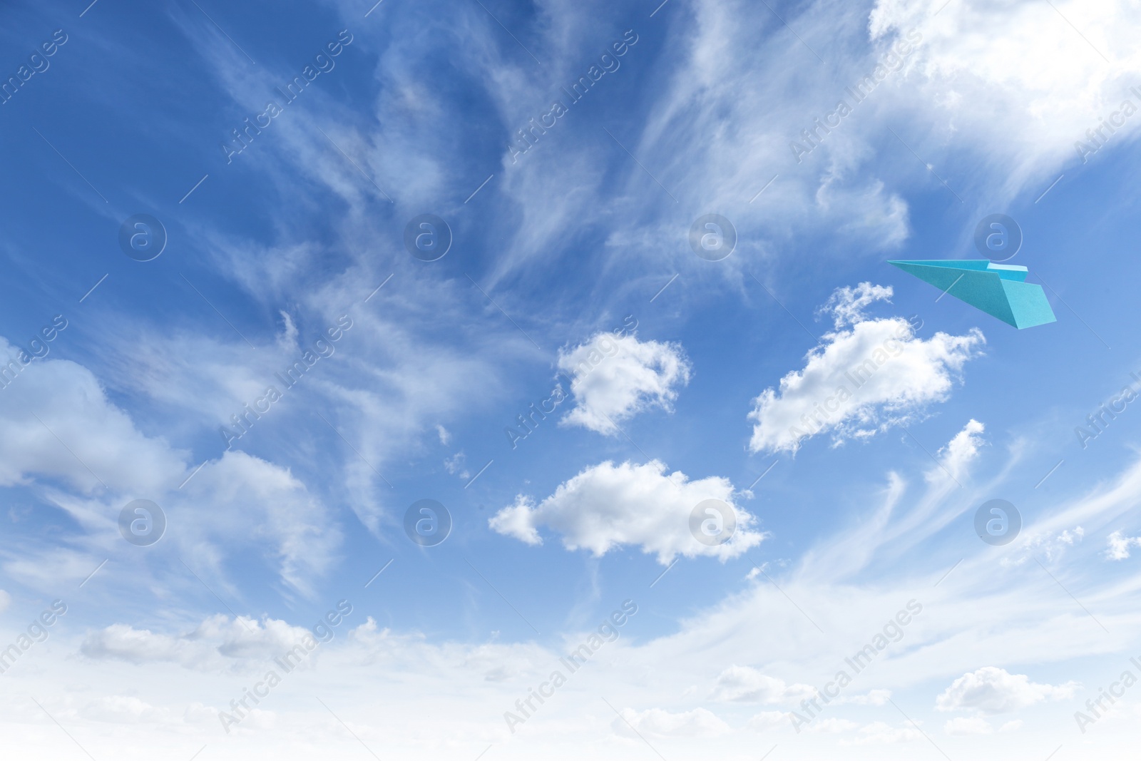 Image of Light blue paper plane flying in sky with clouds with clouds