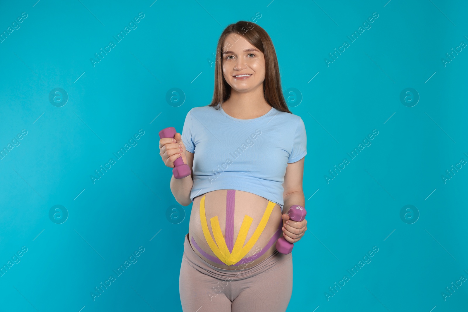 Photo of Pregnant woman with kinesio tapes on her belly doing exercises against light blue background