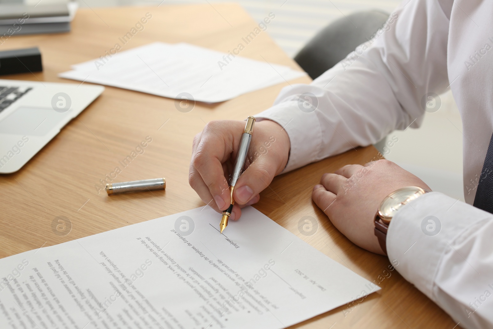 Photo of Notary signing document at wooden table, closeup