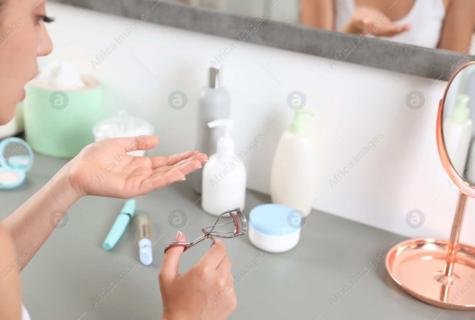 Photo of Young woman holding fallen eyelashes and curler indoors