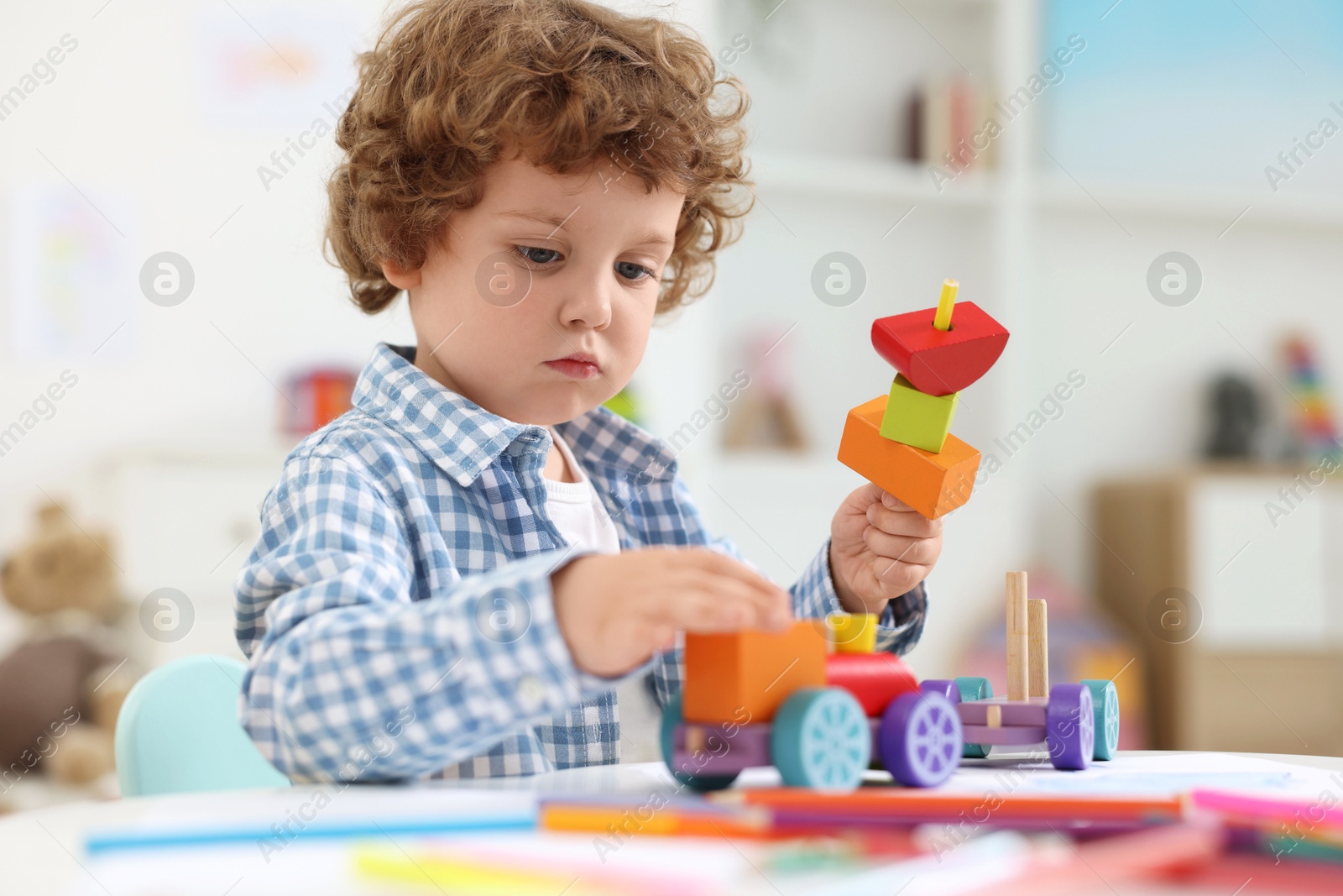 Photo of Cute little boy playing with wooden toys at white table in kindergarten