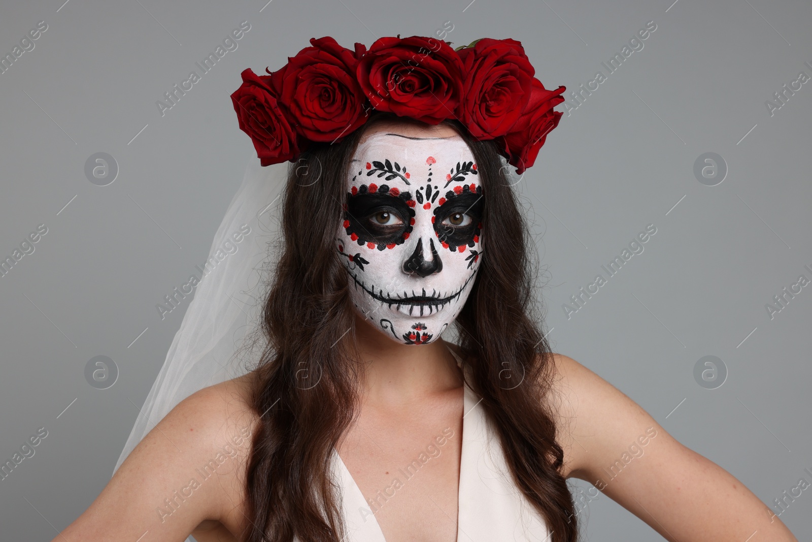 Photo of Young woman in scary bride costume with sugar skull makeup and flower crown on light grey background. Halloween celebration