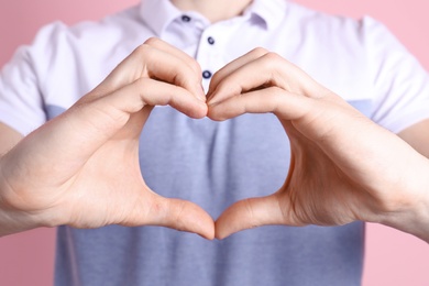 Photo of Young man making heart with his hands on color background, closeup