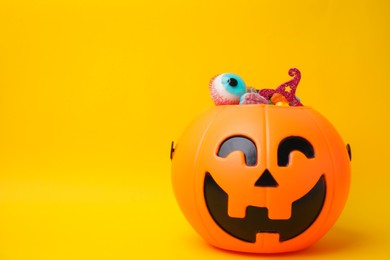 Photo of Halloween trick or treat bucket with different sweets on yellow background, space for text