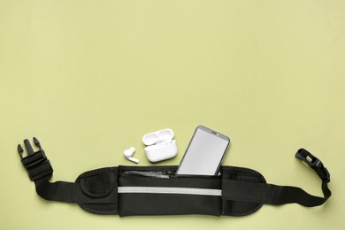 Photo of Stylish black waist bag with smartphone and earphones on green background, flat lay. Space for text