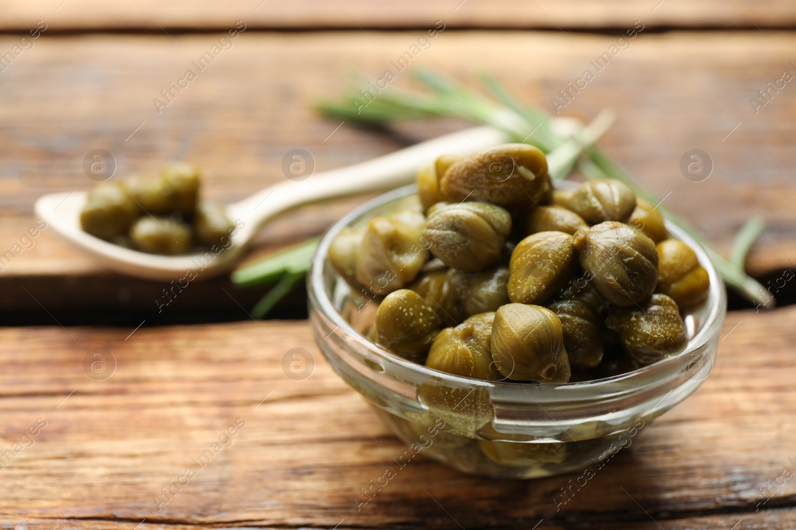 Photo of Tasty capers in glass bowl on wooden table, closeup. Space for text