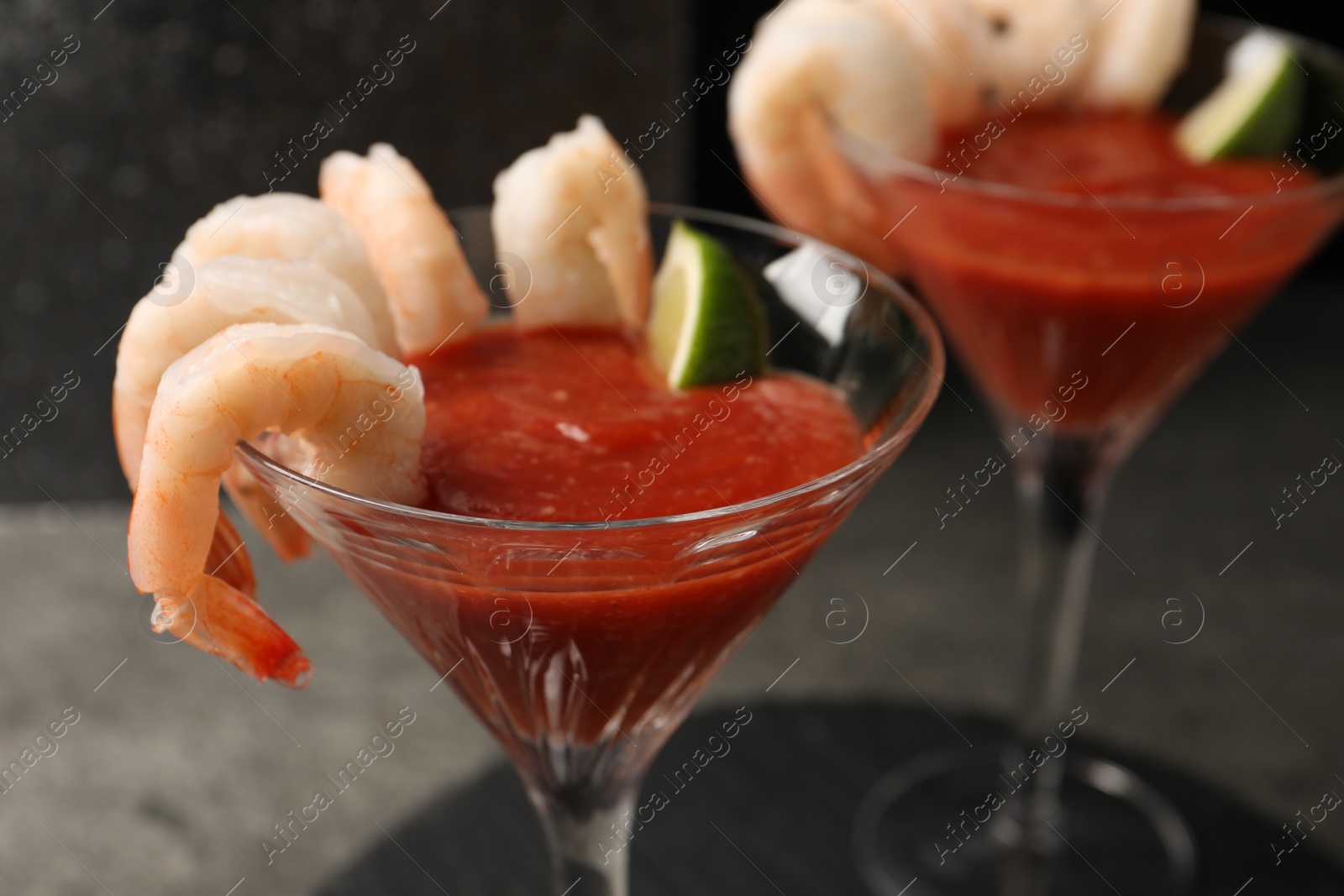 Photo of Tasty shrimp cocktail with sauce and lime in glasses on grey table, closeup