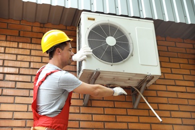 Photo of Male technician fixing air conditioner outdoors