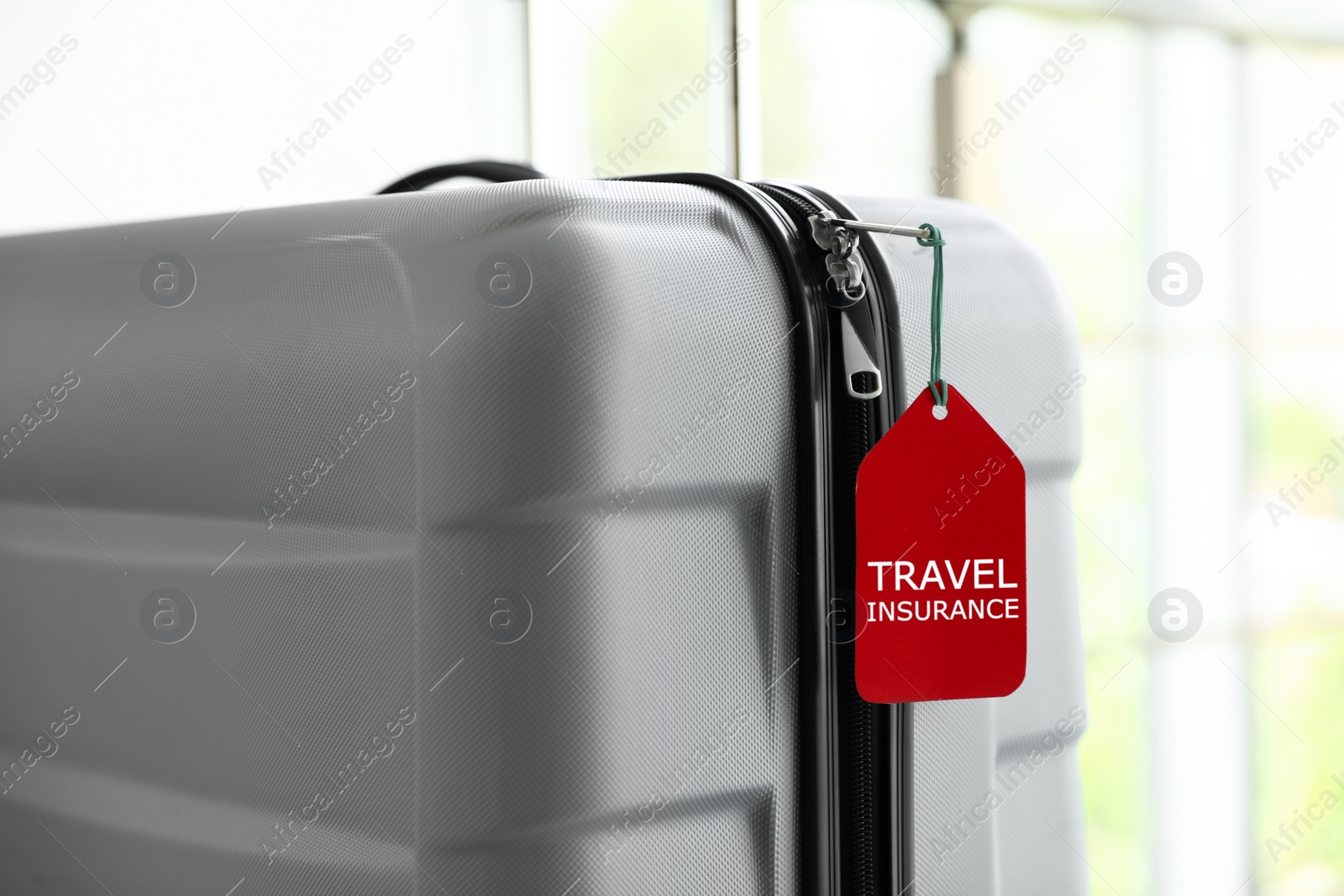 Photo of Stylish suitcase with travel insurance label on blurred background, closeup. Space for text