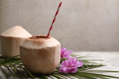 Photo of Young peeled coconuts with straw, palm leaf and beautiful flowers on grey table. Space for text