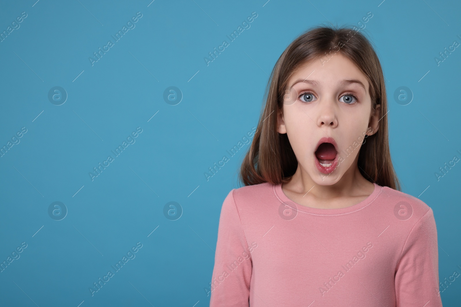 Photo of Portrait of surprised girl on light blue background. Space for text