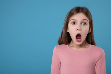 Portrait of surprised girl on light blue background. Space for text