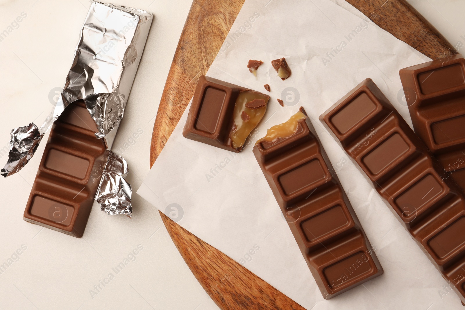 Photo of Tasty chocolate bars with wooden board on white table, flat lay