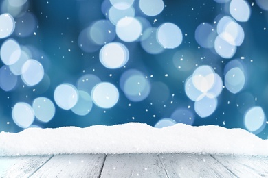 Image of Wooden surface with heap of snow and blurred Christmas lights on background, bokeh effect 