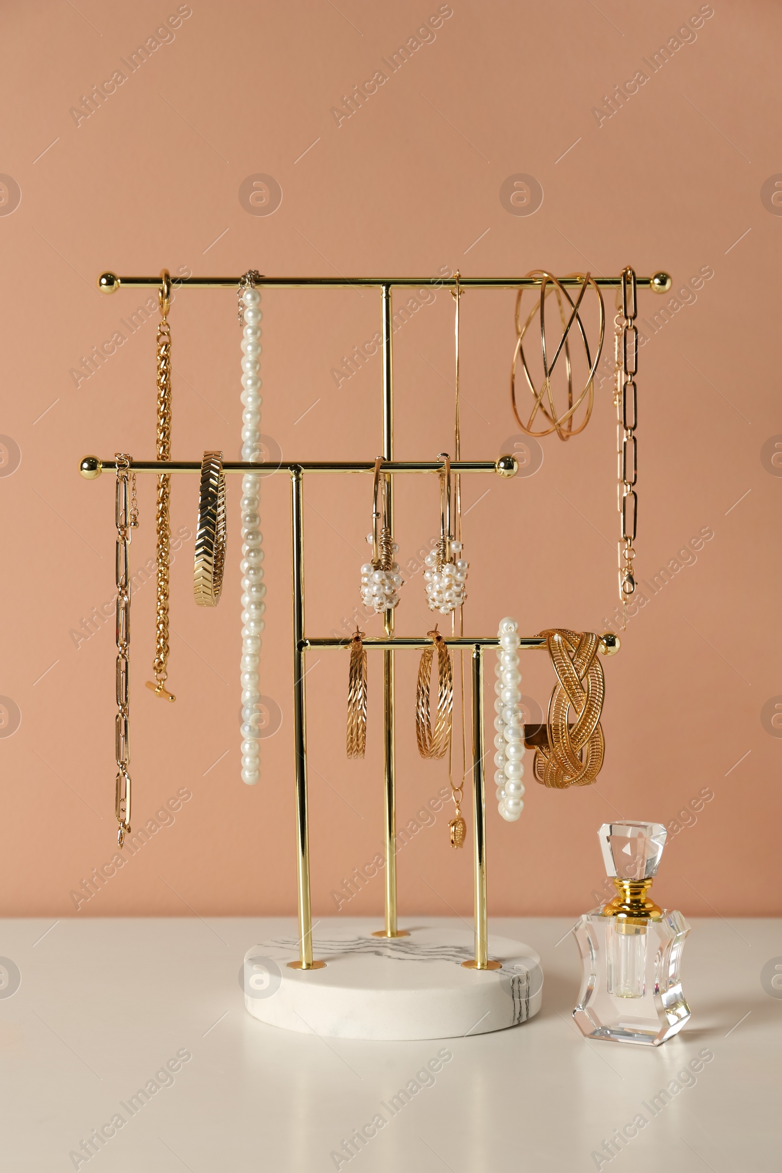 Photo of Holder with set of luxurious jewelry and perfume on white table near pale pink wall