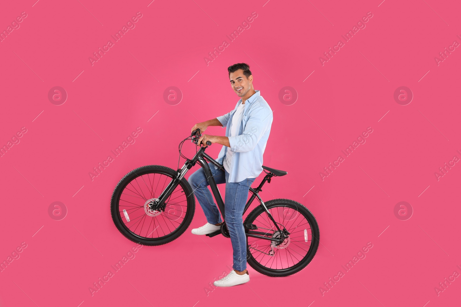 Photo of Handsome young man with modern bicycle on pink background