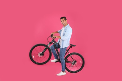 Handsome young man with modern bicycle on pink background