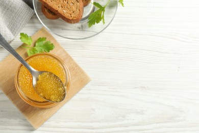 Photo of Fresh pike caviar in glass jar, parsley, bread and spoon on white wooden table, flat lay. Space for text