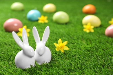 Ceramic Easter bunnies and dyed eggs on green grass, space for text