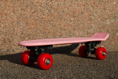Pink skateboard with red wheels on asphalt outdoors