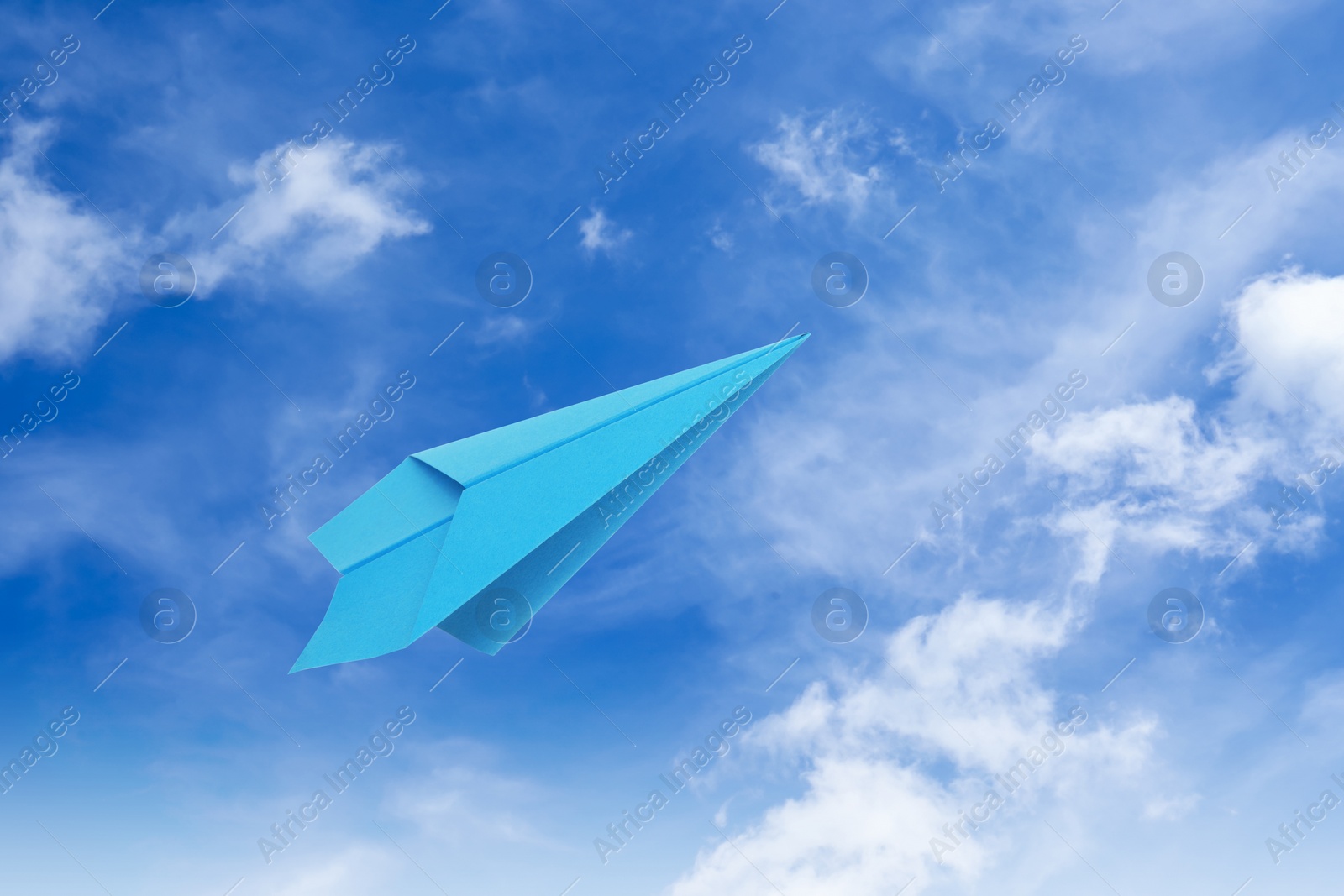 Image of Light blue paper plane flying in sky with clouds with clouds