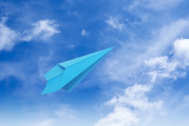 Image of Light blue paper plane flying in sky with clouds with clouds