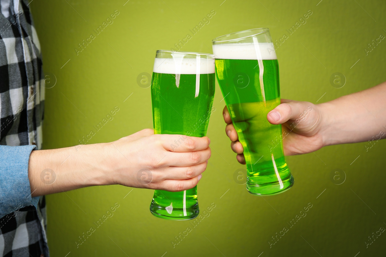 Photo of Man and woman toasting with green beer on color background, closeup. St. Patrick's Day celebration