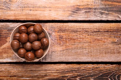 Delicious organic Macadamia nuts in bowl on wooden table, top view. Space for text