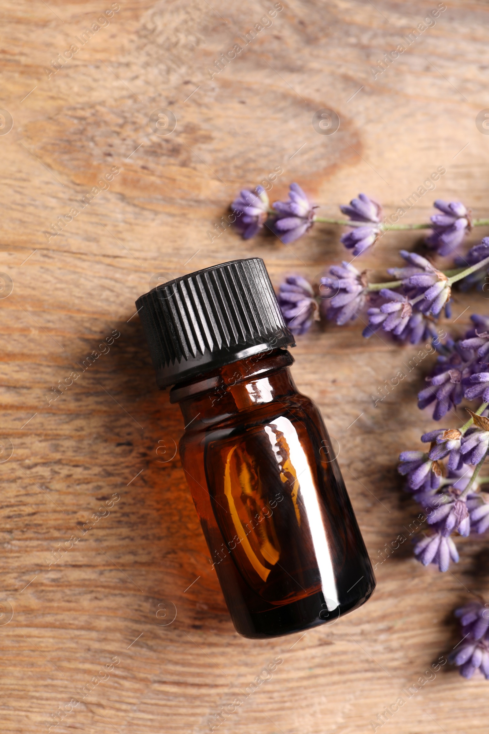 Photo of Bottle of essential oil and lavender flowers on wooden table, flat lay
