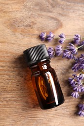 Bottle of essential oil and lavender flowers on wooden table, flat lay