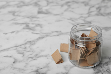 Photo of Glass jar with paper pieces on white marble table, space for text