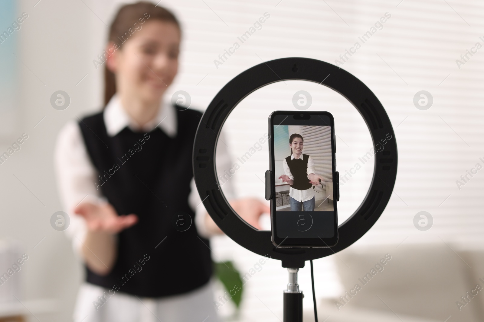 Photo of Teenage blogger explaining something while streaming at home, focus on smartphone