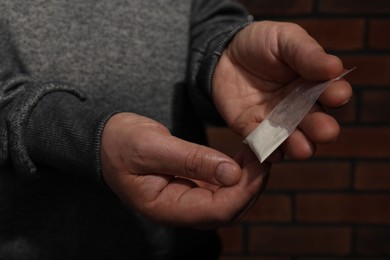 Photo of Drug addiction. Man with plastic bag of cocaine on blurred background, closeup