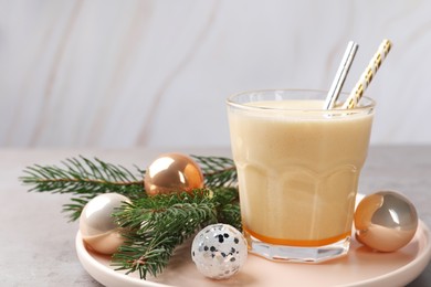 Glass of delicious eggnog and decorated fir branch on gray table, space for text