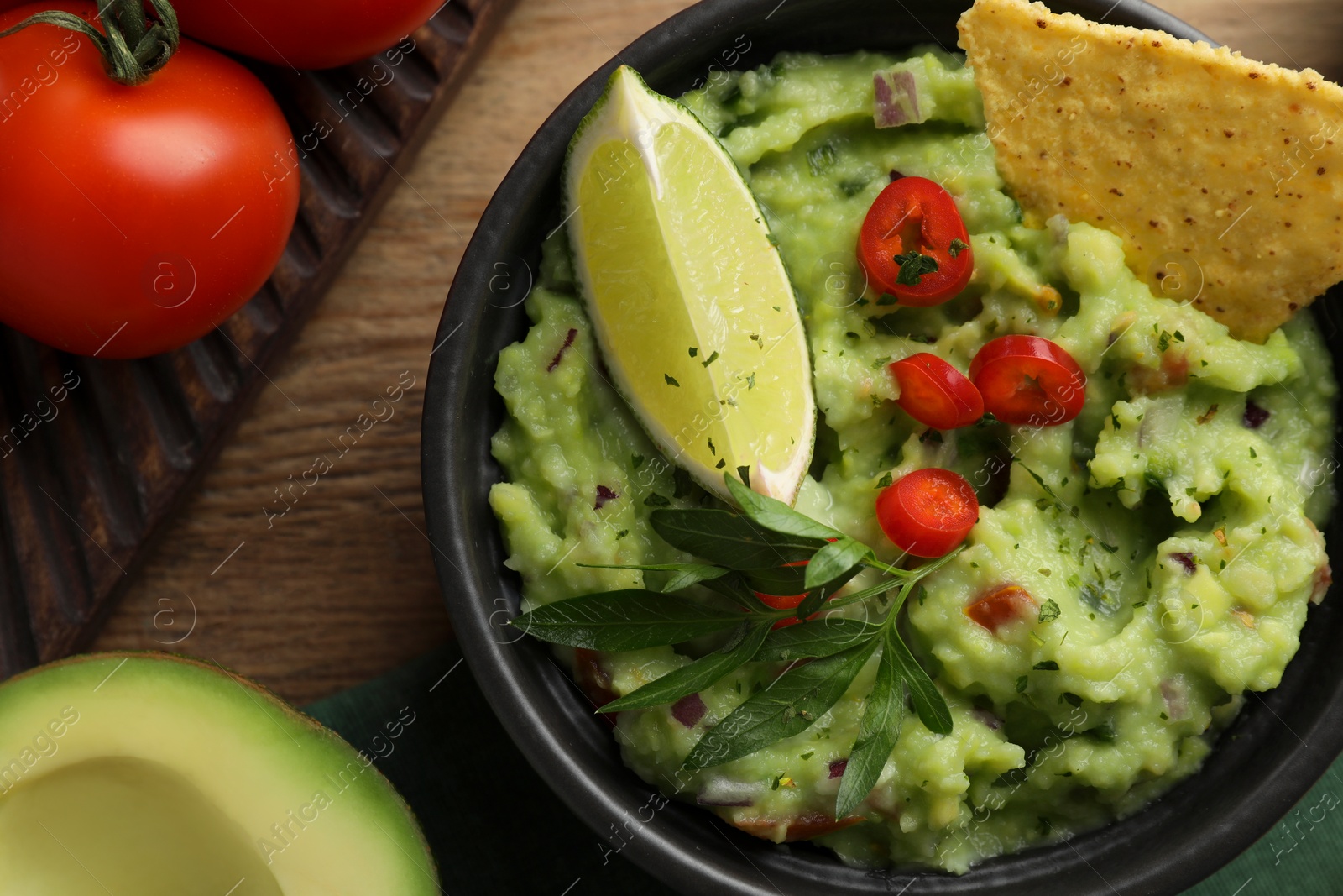 Photo of Delicious guacamole with nachos chips and ingredients on wooden table, flat lay