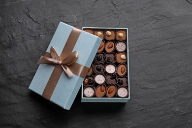 Photo of Open box of delicious chocolate candies on black table, top view