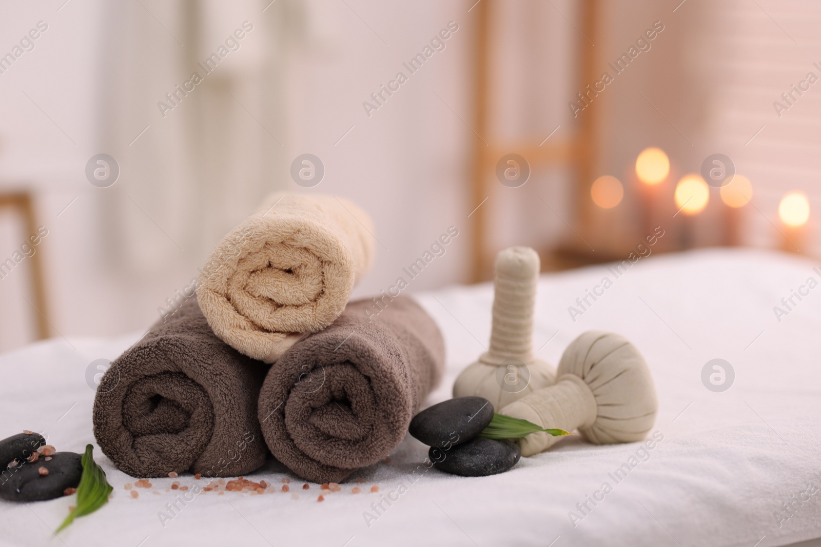 Photo of Spa stones, rolled towels and herbal bags on massage table indoors