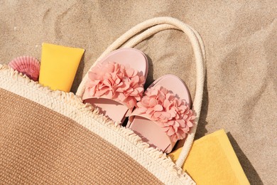Photo of Stylish bag with beach accessories on sand, top view