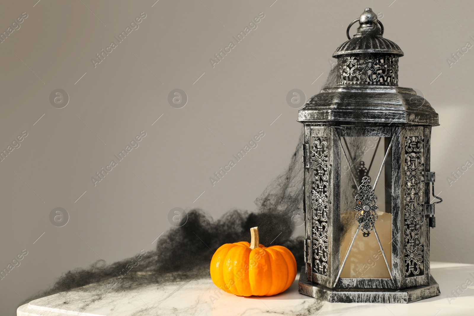 Photo of Lantern, pumpkin and black cobweb on table near grey wall, space for text. Halloween decor