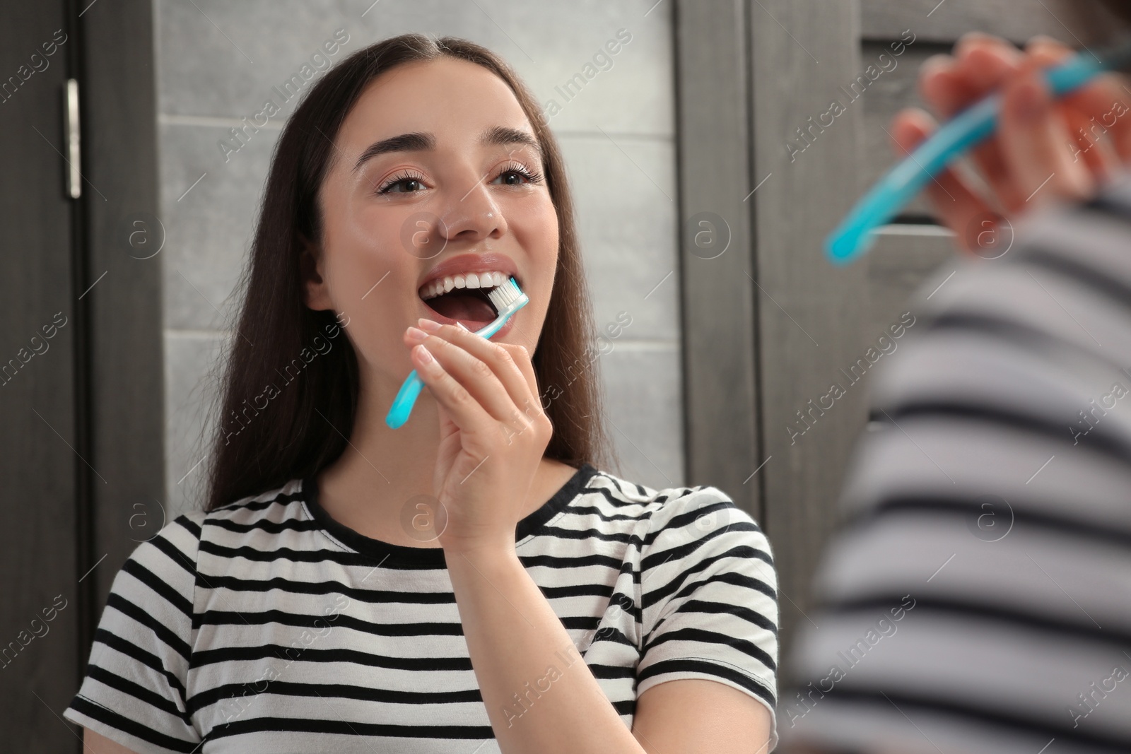 Photo of Young woman brushing her teeth with plastic toothbrush near mirror in bathroom