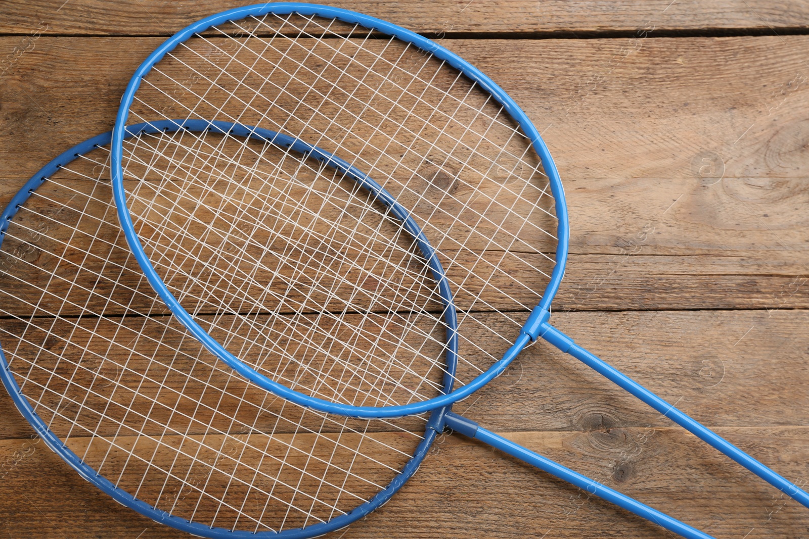 Photo of Rackets on wooden table, flat lay. Badminton equipment