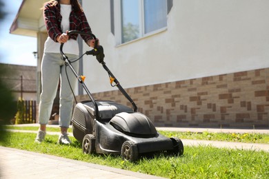 Woman cutting green grass with lawn mower on backyard, closeup